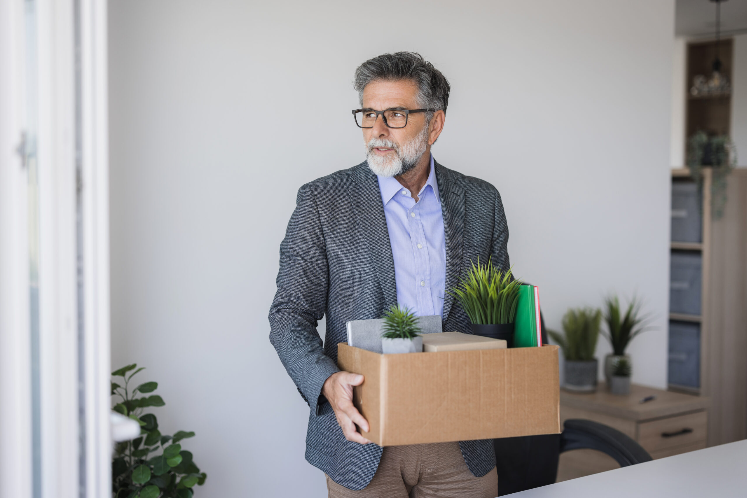 Sad fired mature manager leaving office holding a box with his belongings